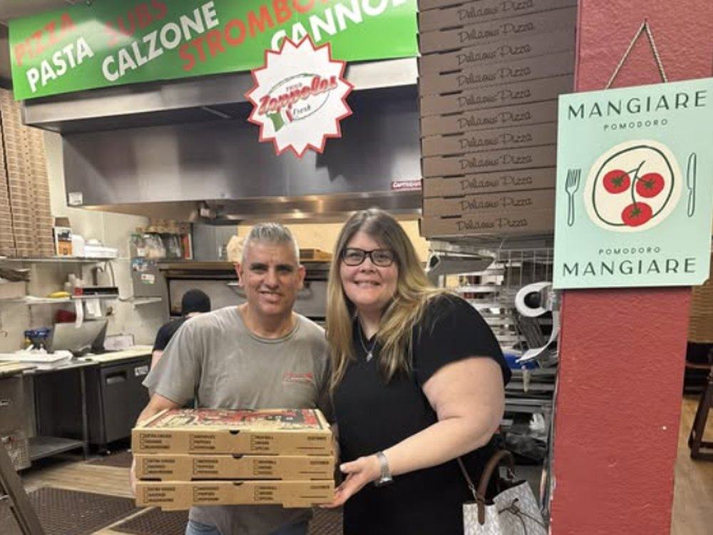 Carlos handing a stack of fresh pizzas to a happy customer at Pomodoro