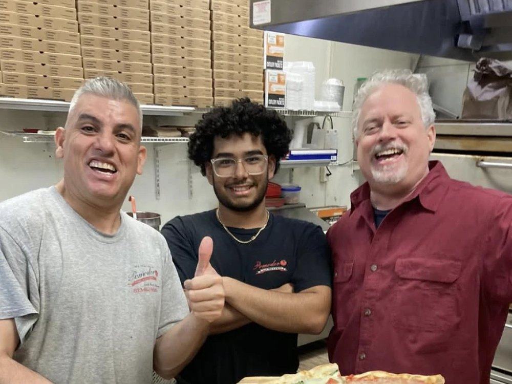 Carlos and the Pomodoro team smiling in the kitchen with a fresh pizza